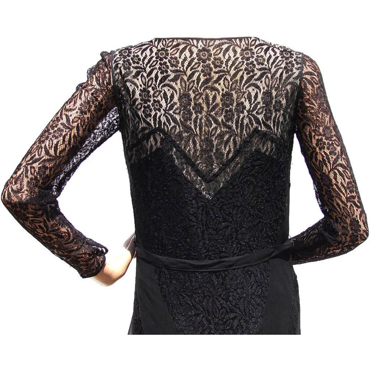 close up of vintage 1930s black lace long-sleeve dress shown from the back, featuring an intricate floral lace pattern across the upper back, sleeves, and bodice, with a solid black silk chiffon fabric lower section and a matching waist tie.
