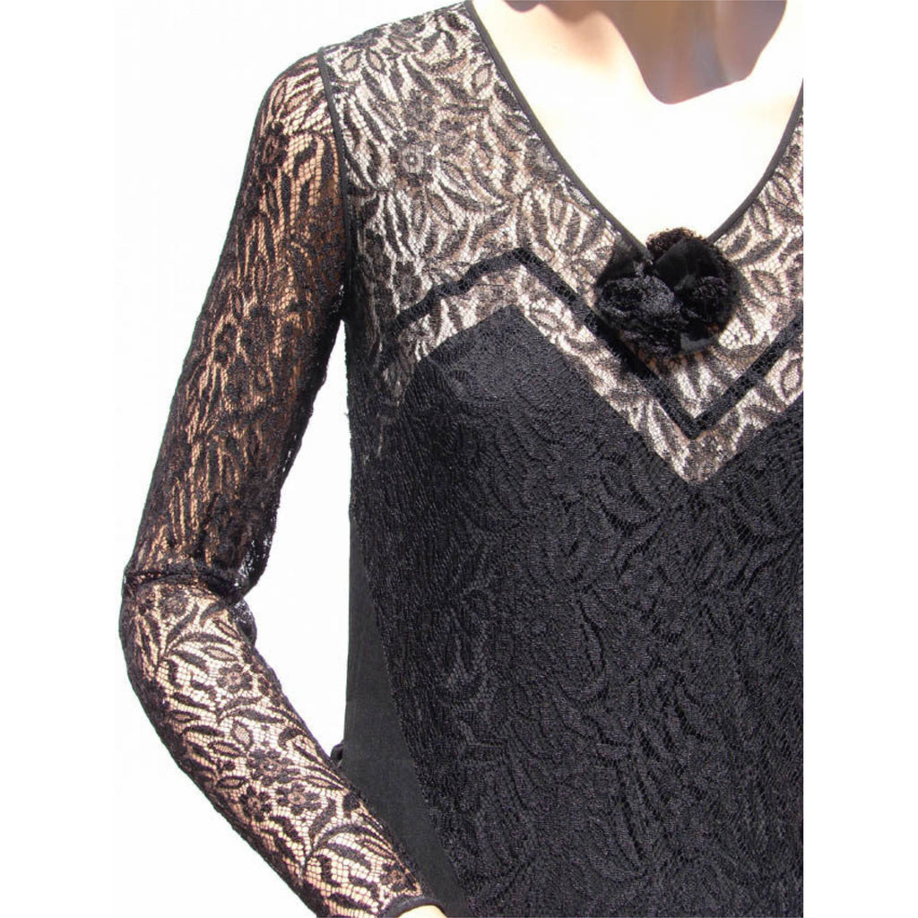A close-up of a 1930s black lace long-sleeve dress with a fuzzy black pom-pom detail at the neckline