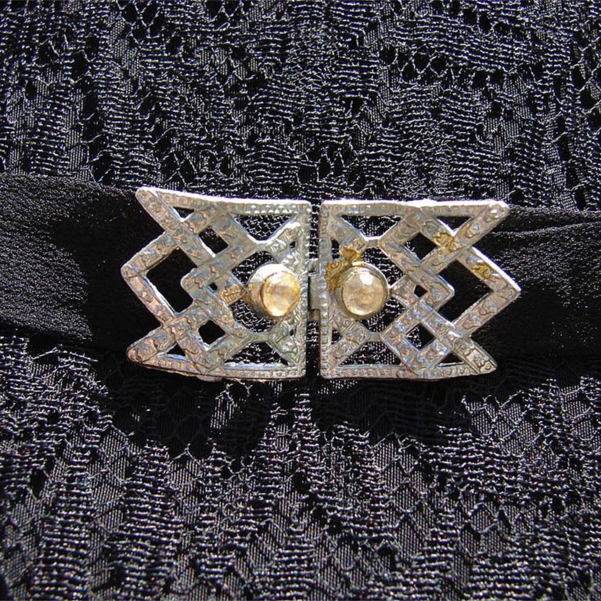 A close-up of a vintage silver filigree belt buckle on a 1930s dress