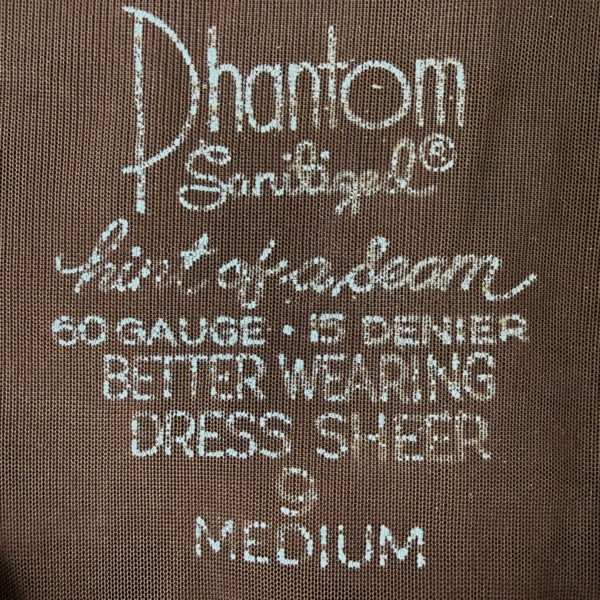 Close-up of a brown nylon stocking reading 'Phantom Sanitized Hint of a Seam 60 GAUGE • 15 DENIER BETTER WEARING DRESS SHEER 9 MEDIUM'.