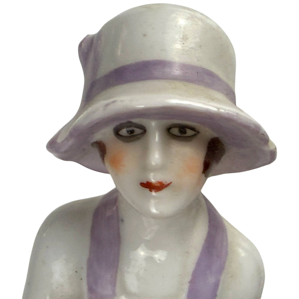 Close-up of 1920s porcelain half-doll face with painted eyes, rouged cheeks, red lips and lavender cloche hat