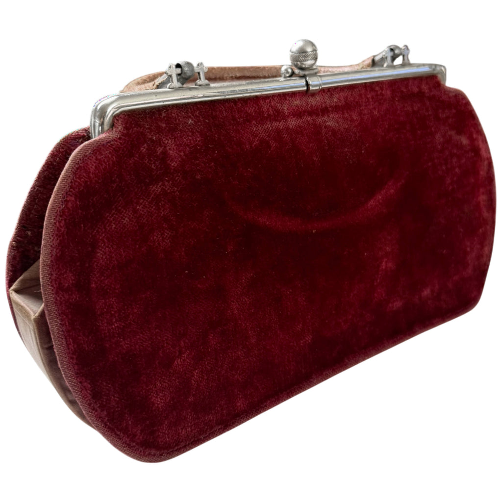 Angled view of antique Edwardian burgundy velvet handbag showing rounded body, metal frame and leather handle
