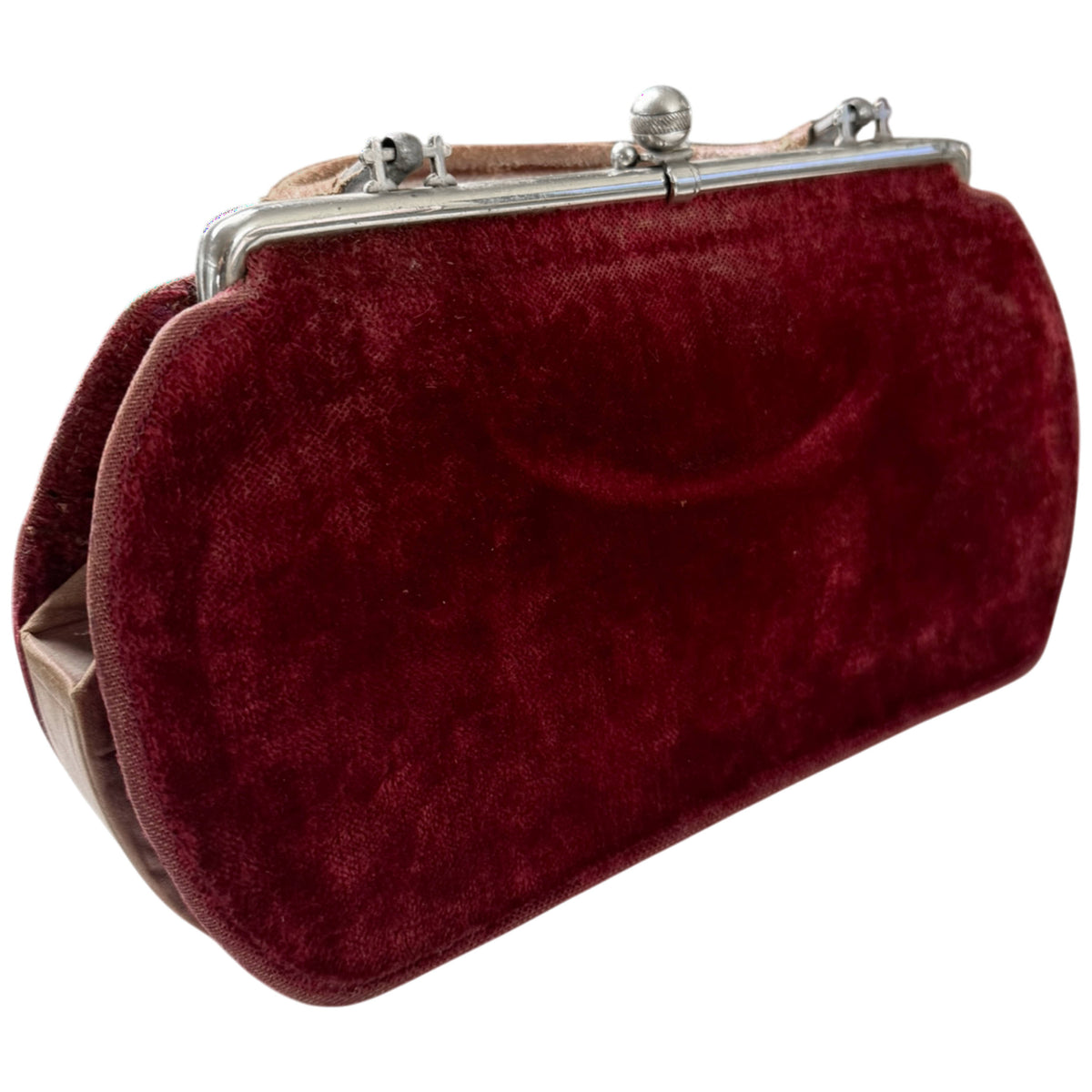 Angled view of antique Edwardian burgundy velvet handbag showing rounded body, metal frame and leather handle