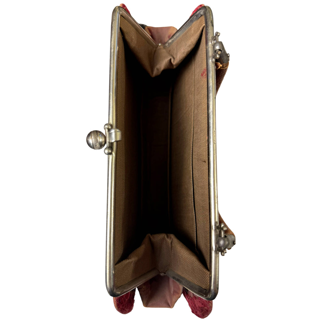 Overhead view inside antique burgundy velvet handbag showing metal frame, gathered gussets and tan fabric lining