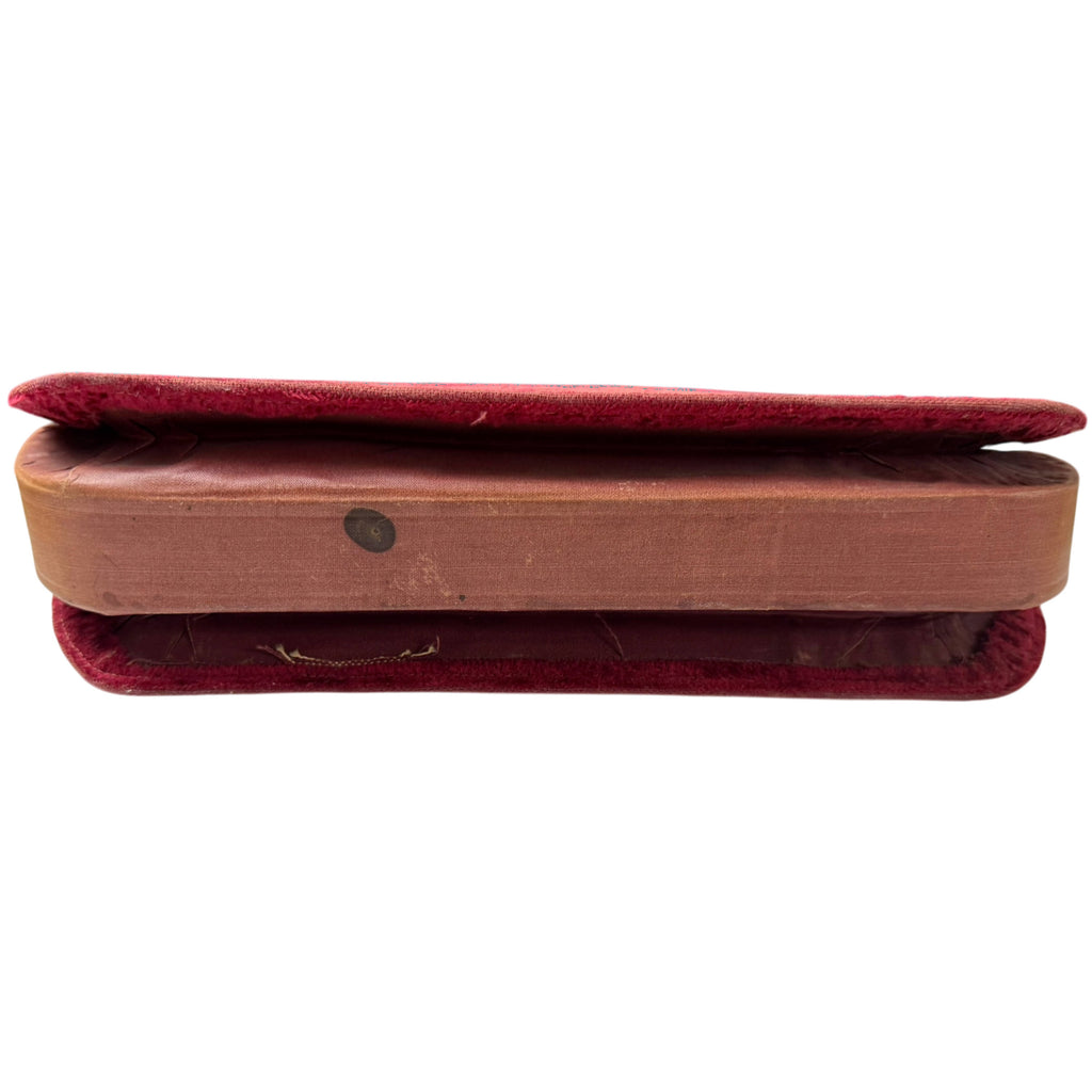 Underside of antique burgundy velvet handbag showing round stain and signs of age-related wear