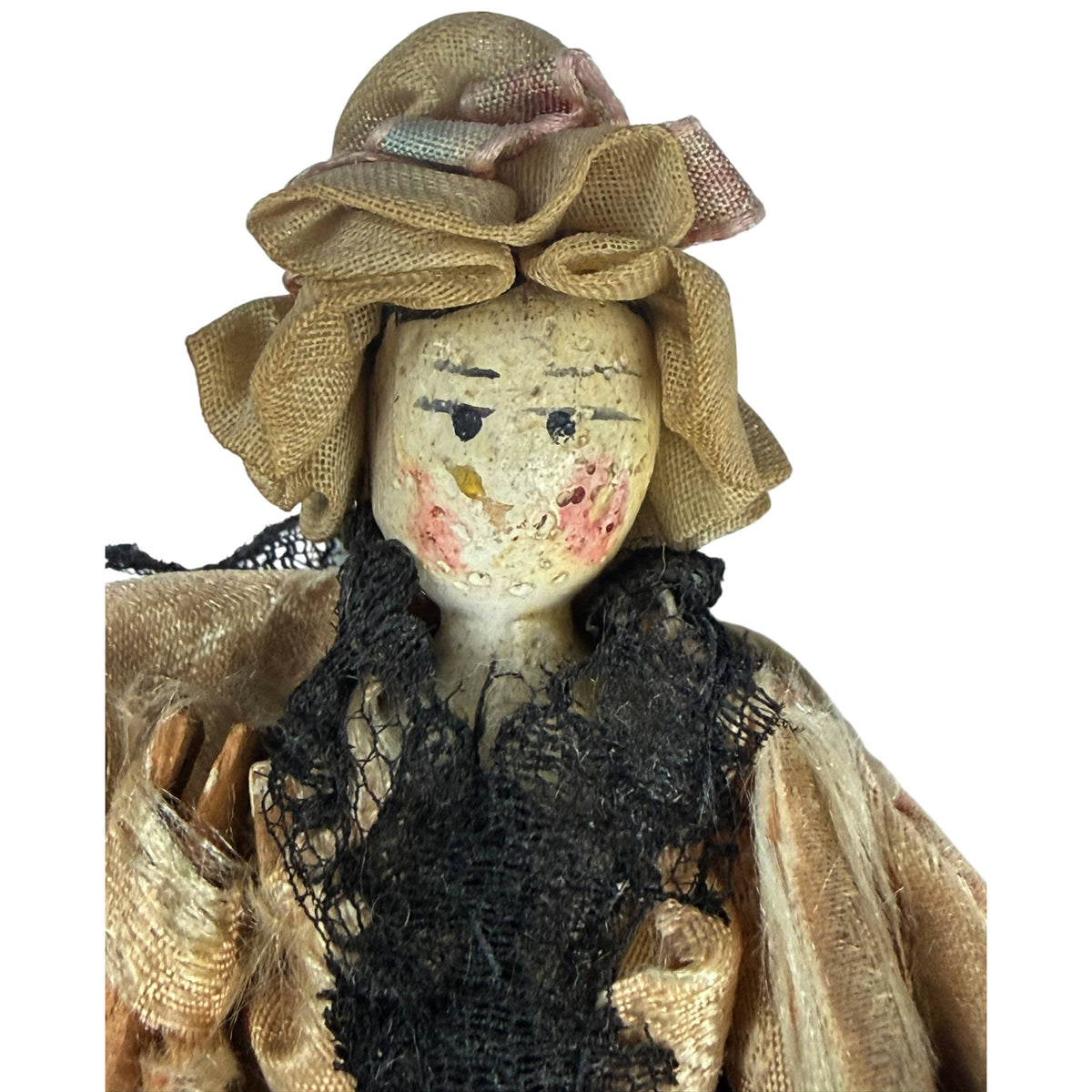 Close-up of antique Grödnertal wooden doll's painted face, fabric bonnet, faded ribbons and black lace bodice