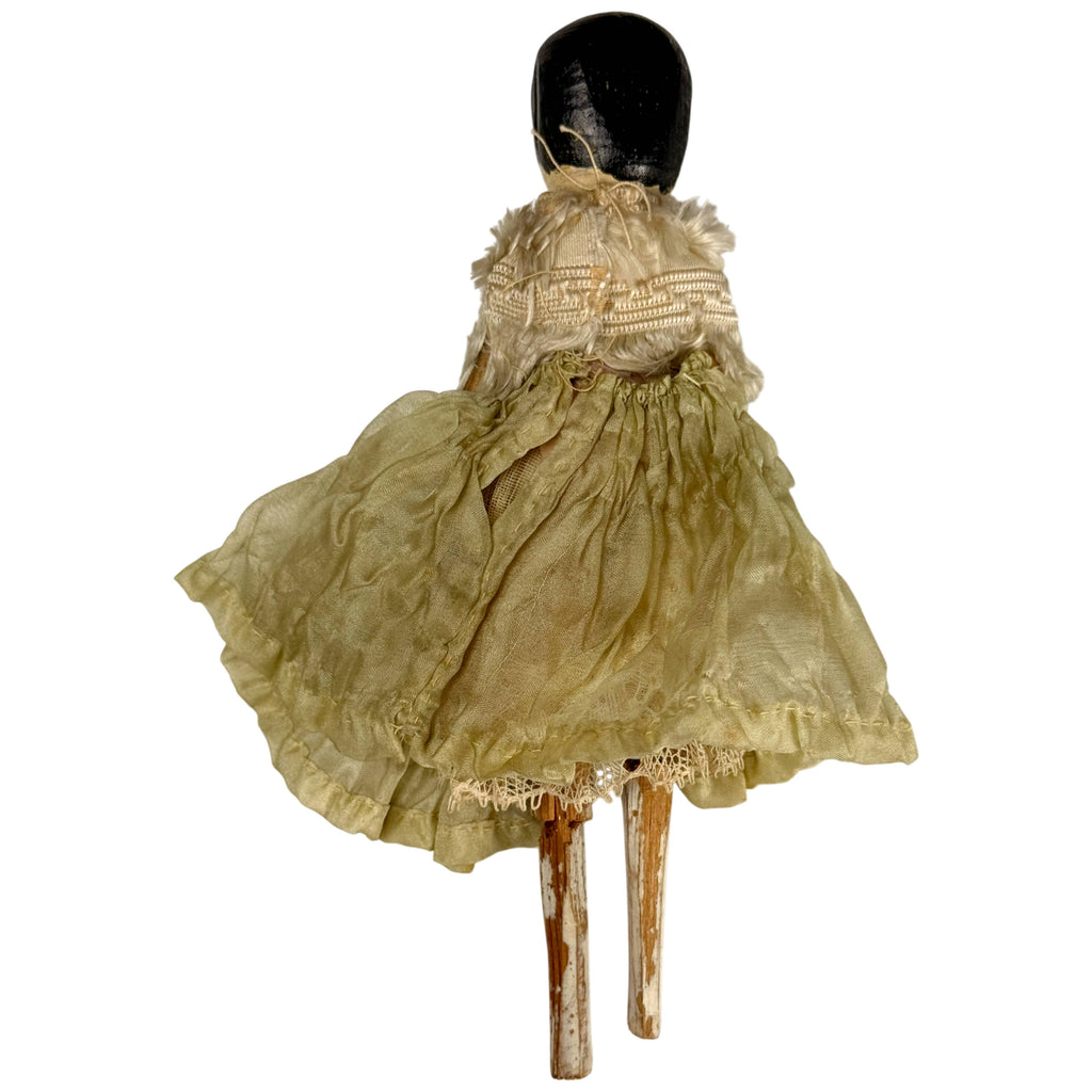 Rear view of antique Grödnertal wooden doll showing black painted hair, silk passementerie and gathered green-toned skirt