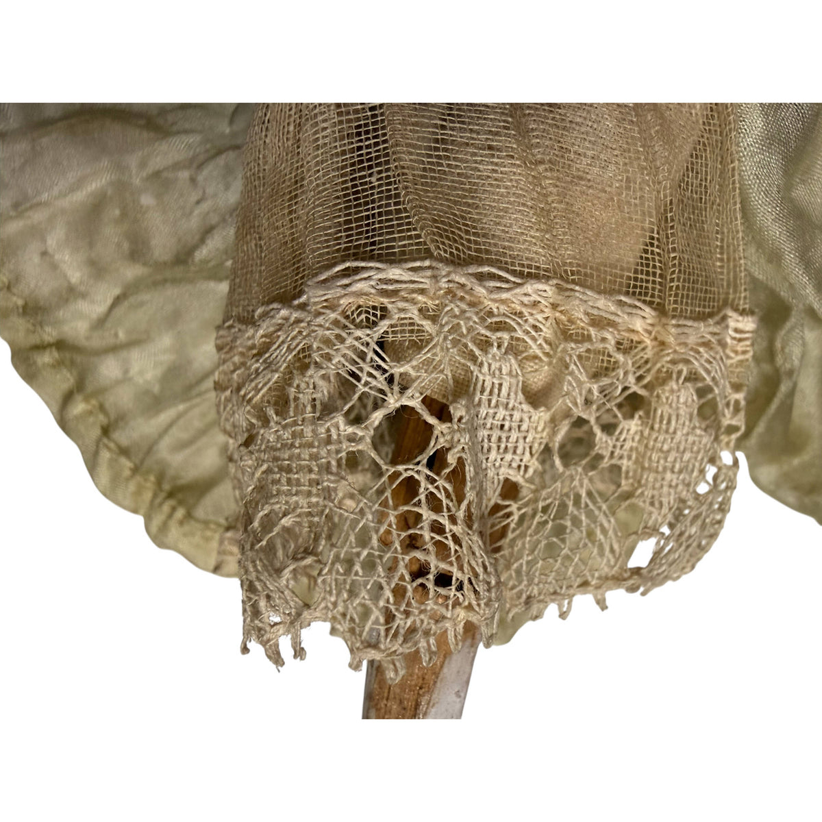 Close-up of delicate openwork lace edging on the antique wooden doll's underskirt, believed to be handmade