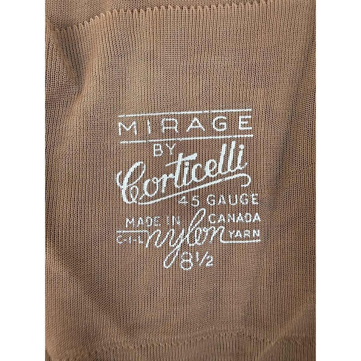 Close-up of a brown nylon stocking with white printed text that reads 'MIRAGE BY Corticelli 45 GAUGE MADE IN CANADA C.I.L. nylon YARN 8 1/2'.