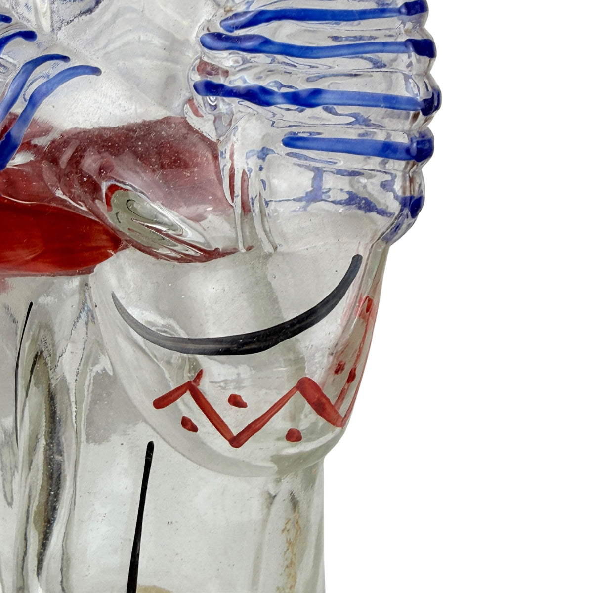 Close-up of a clear glass Cuban drummer figural bottle showing painted details including blue wavy stripes, a black curved line, and red painted accents