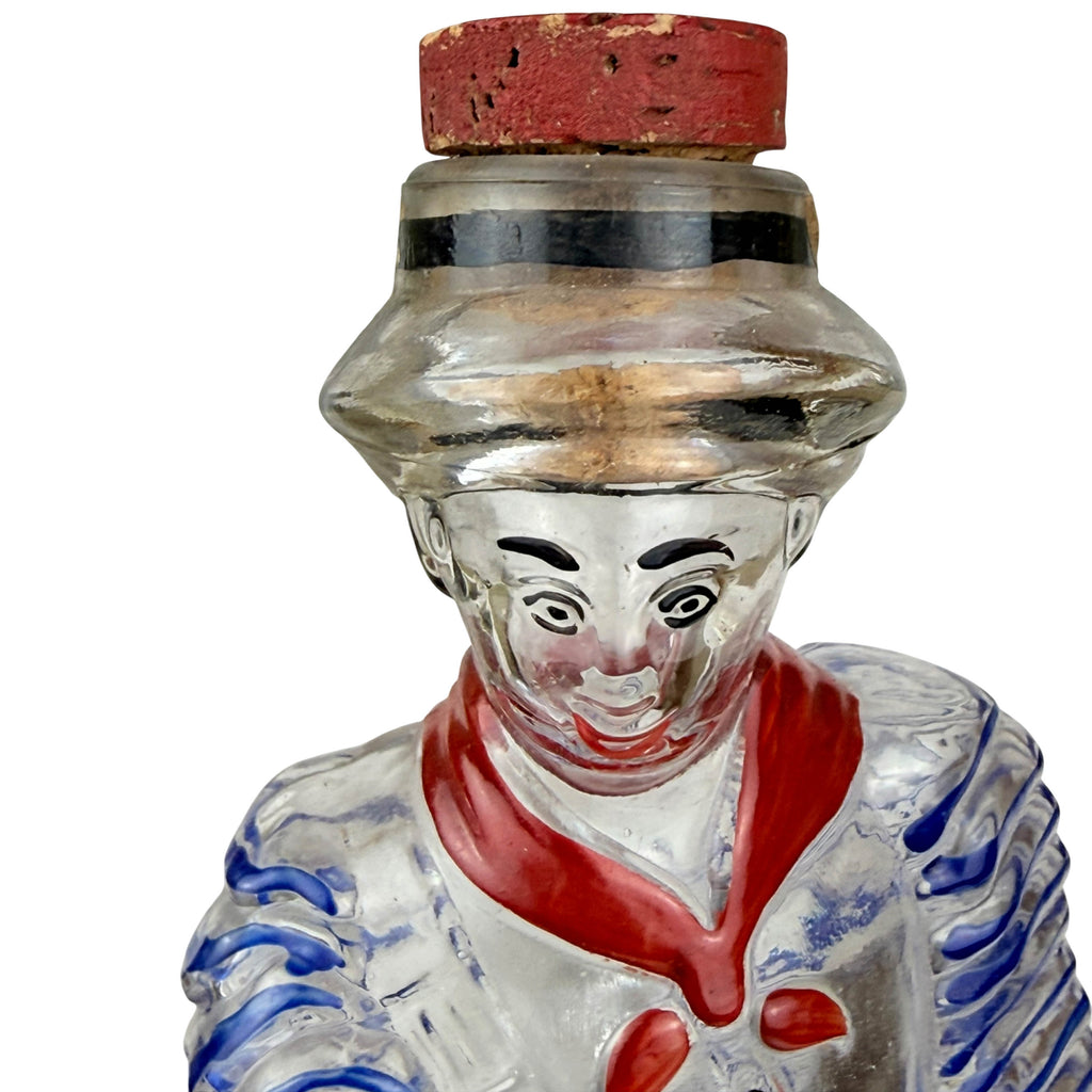 A vintage glass Cuban figural  bottle with a red cork stopper, featuring a painted  face and rumba outfit with red and blue details 