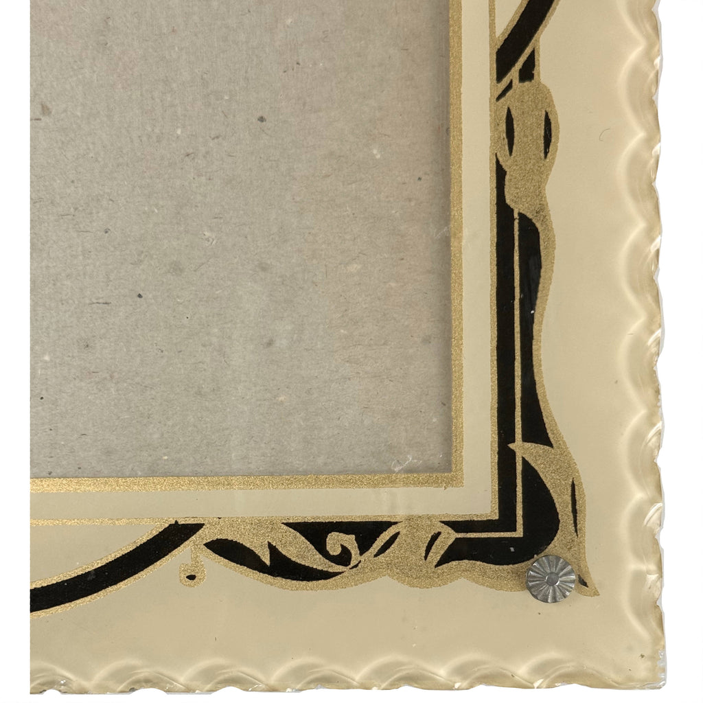 Close-up of 1930s Art Deco glass picture frame showing textured gold scrollwork, black geometric painting, scalloped edge and silver-tone rosette screw.