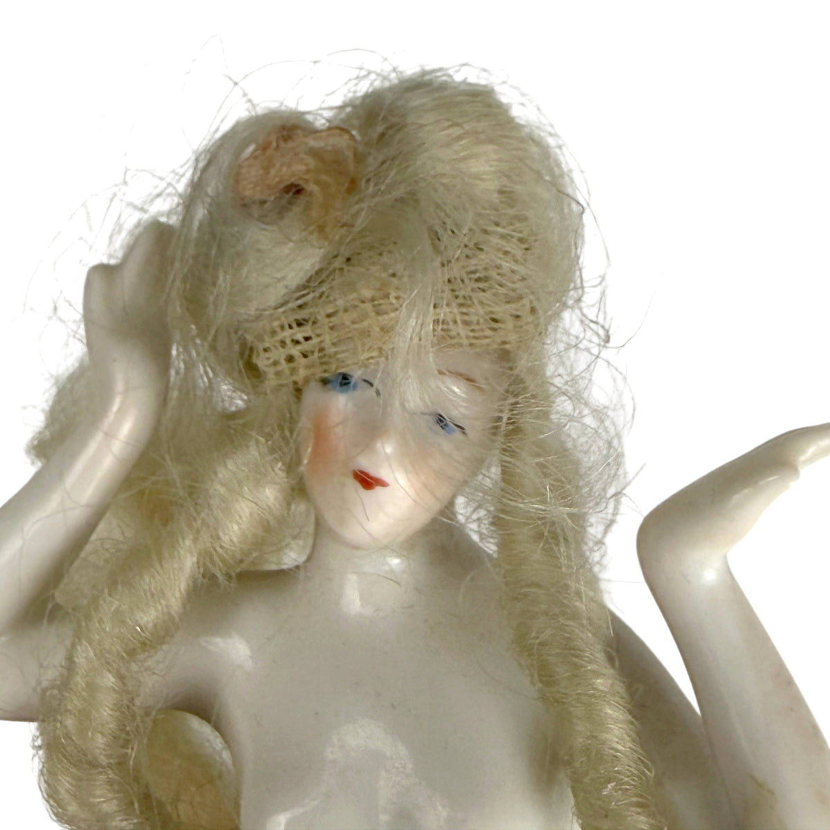 Close-up of antique porcelain half-doll face with painted blue eyes, rosy cheeks and blonde ringlets on net foundation