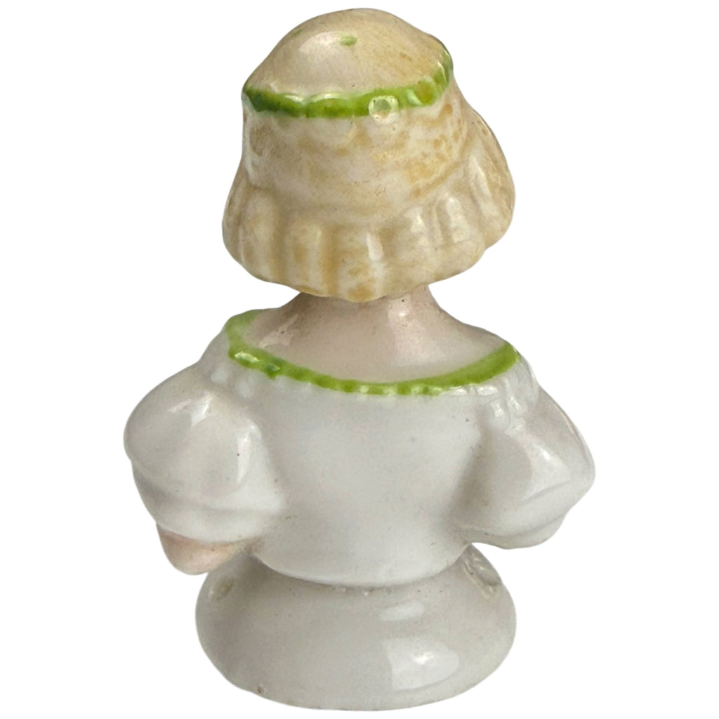 Back view of antique Edwardian-era miniature porcelain half-doll showing blonde bobbed hair, green headband and white puff-sleeve dress