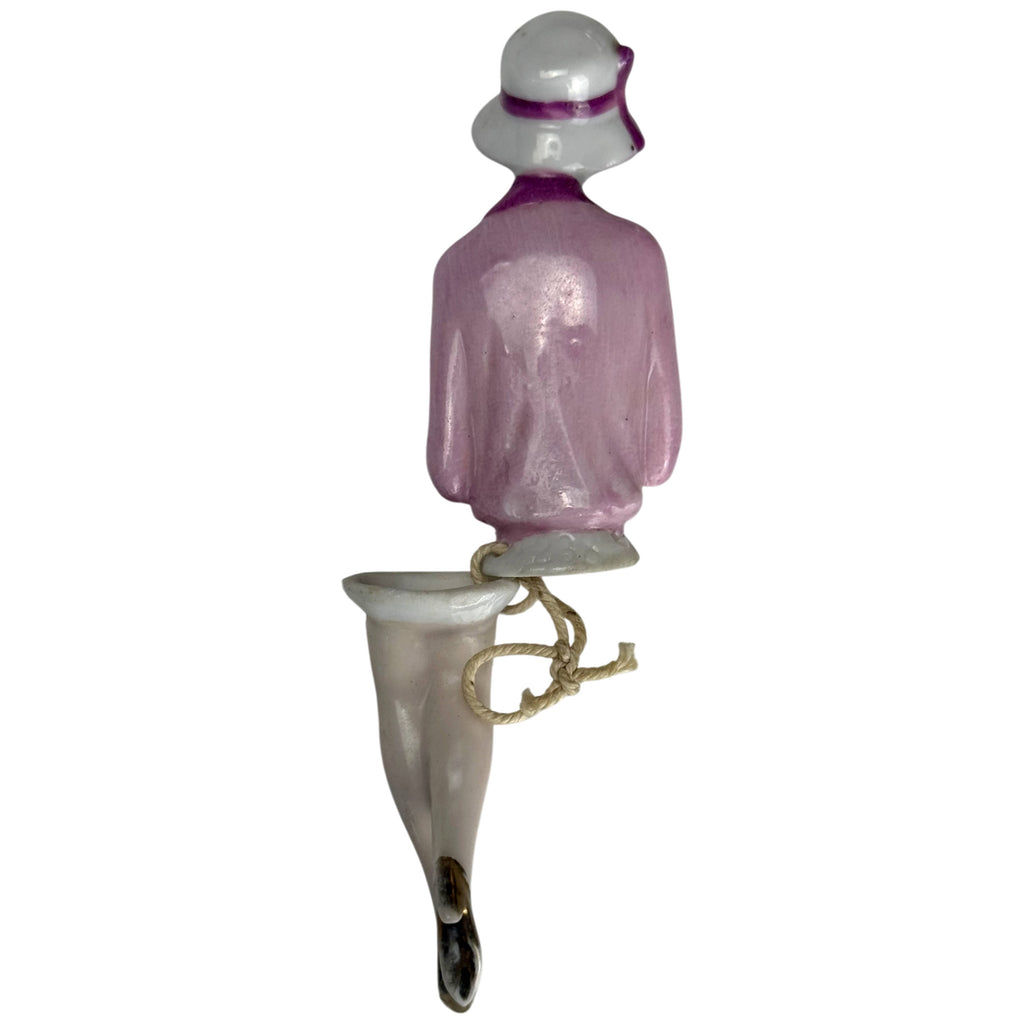 Rear view of antique 1920s porcelain flapper half doll with pink jacket, purple hat trim and attached porcelain legs