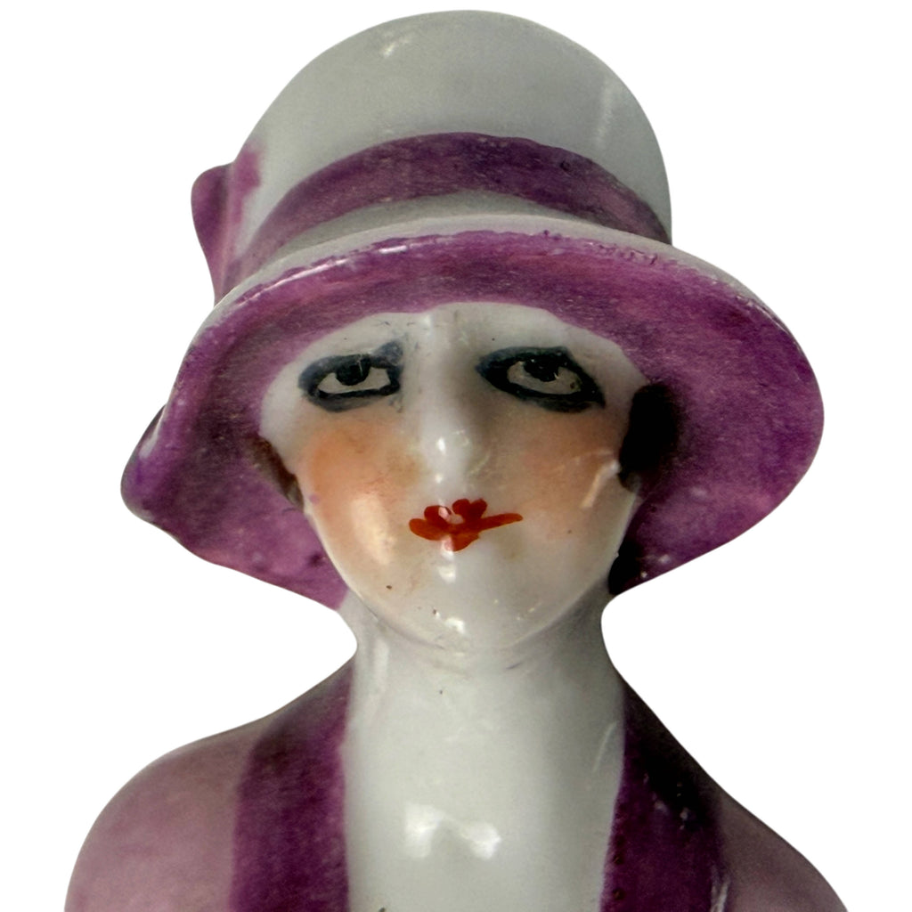 Detailed view of antique porcelain flapper doll face with sideways-glancing eyes, red lips and purple cloche hat