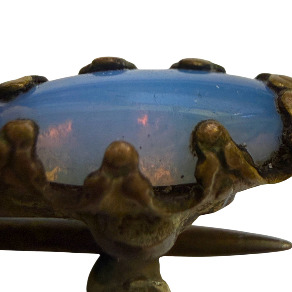 Extreme close-up of blue imitation opal glass cabochon showing pinkish reflections and antique claw prong settings