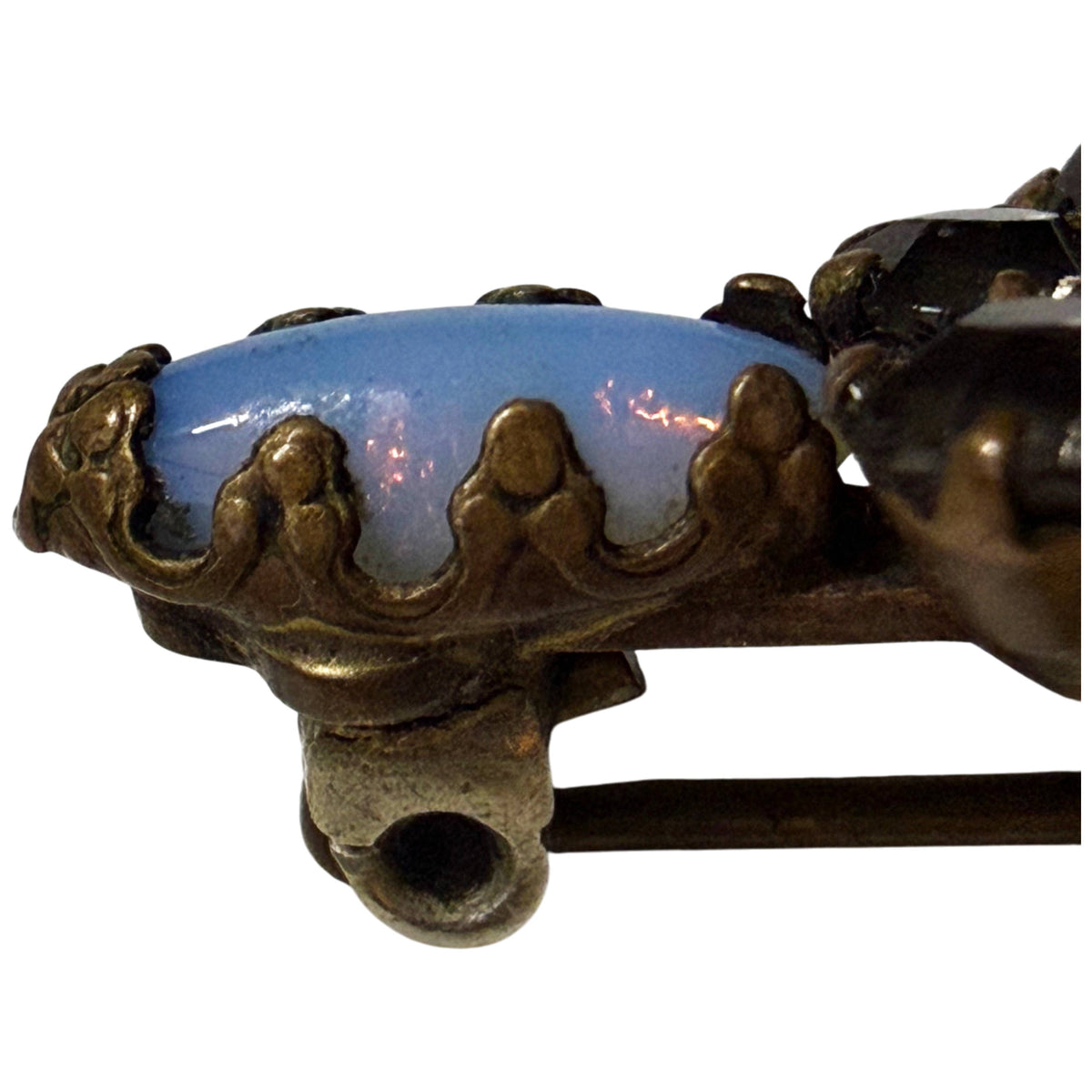 Side close-up of milky blue opalescent glass cabochon, decorative claw prongs and antique pin fitting