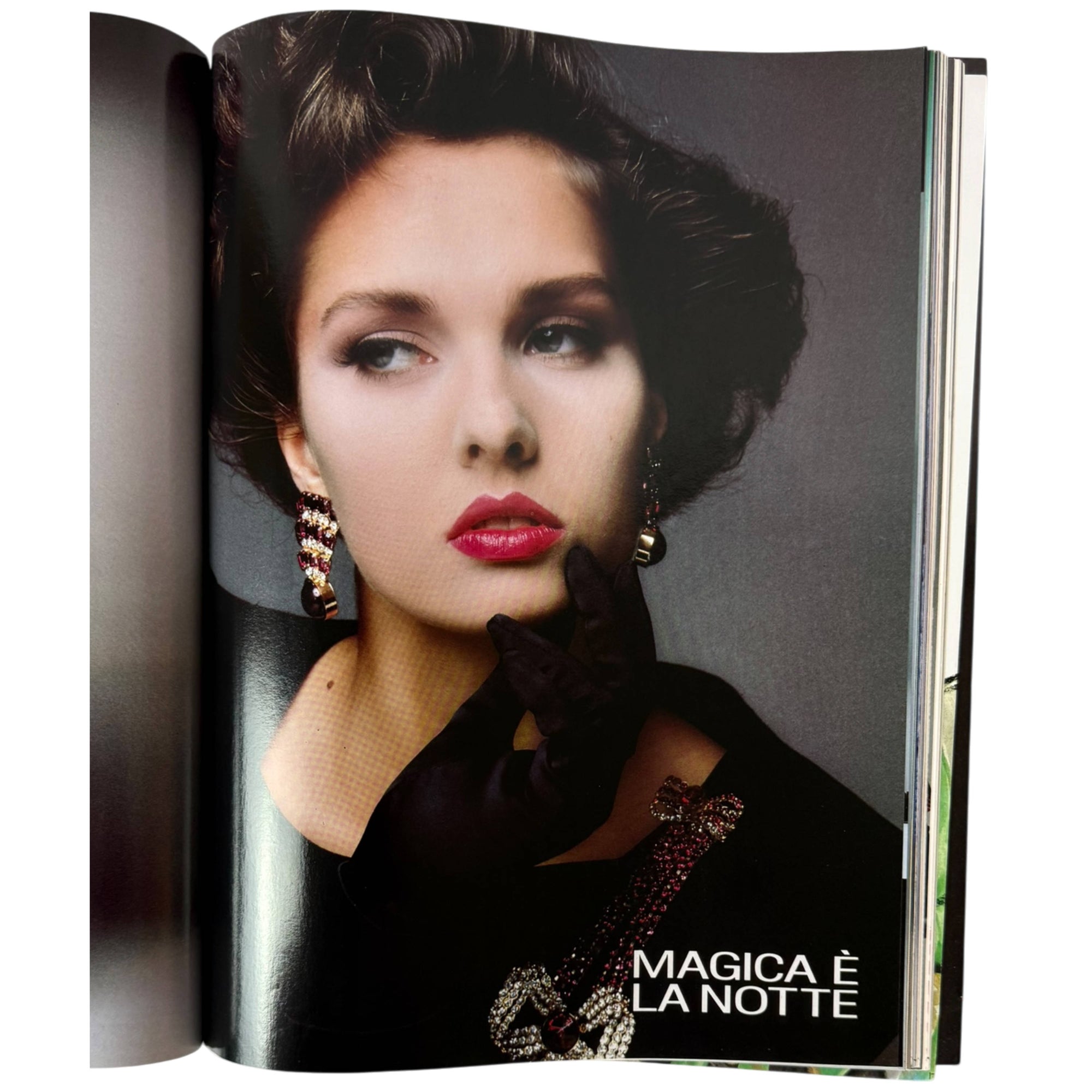 An open harper's bazaar Valentino special magazine showing a fashion portrait page with a woman in a black outfit, red lipstick, and the Italian text 'MAGICA È LA NOTTE' at the bottom right.