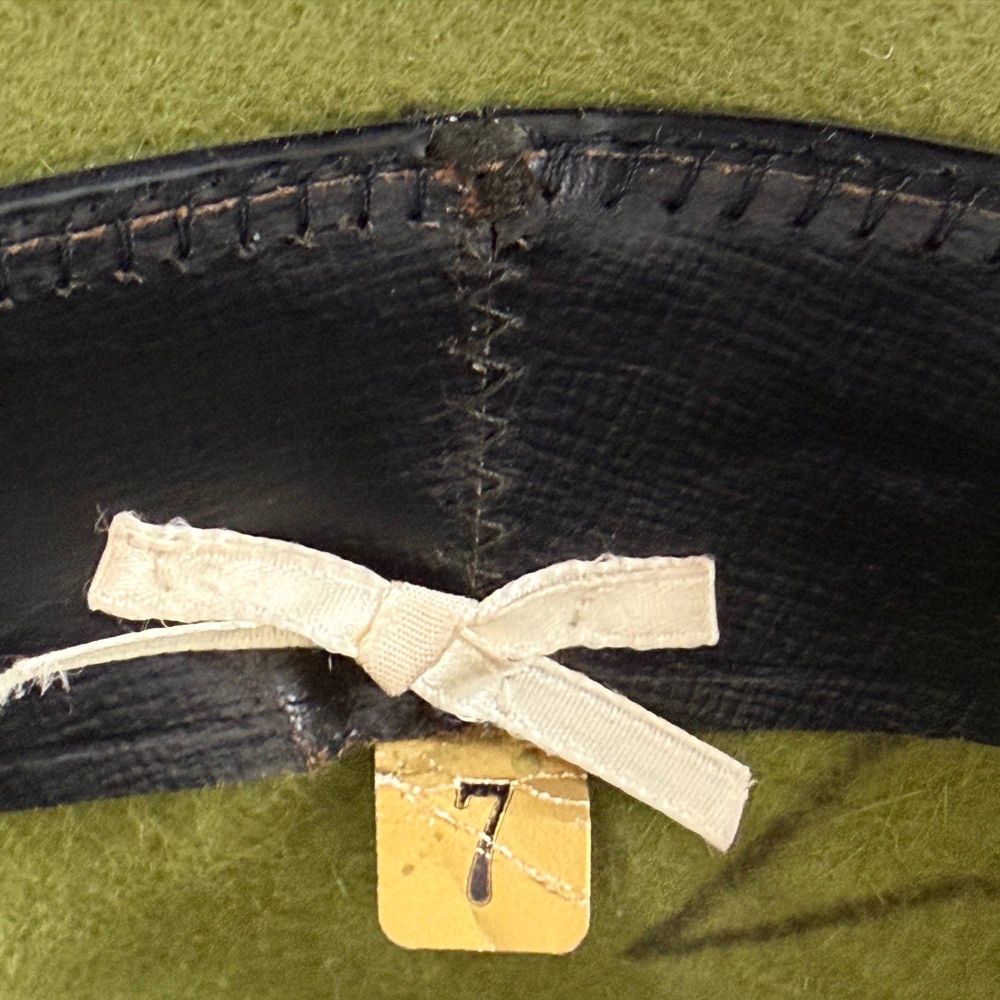 Close-up of a greem hat with a white ribbon and gold tag on a black sweatband