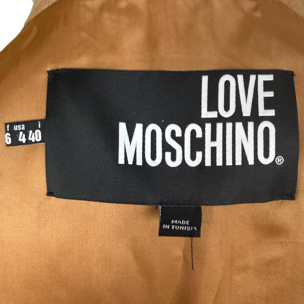 Close-up of a black Love Moschino brand label sewn onto a tan satin coat lining, with a size tag on the left and a small 'Made in Tunisia' tag below.