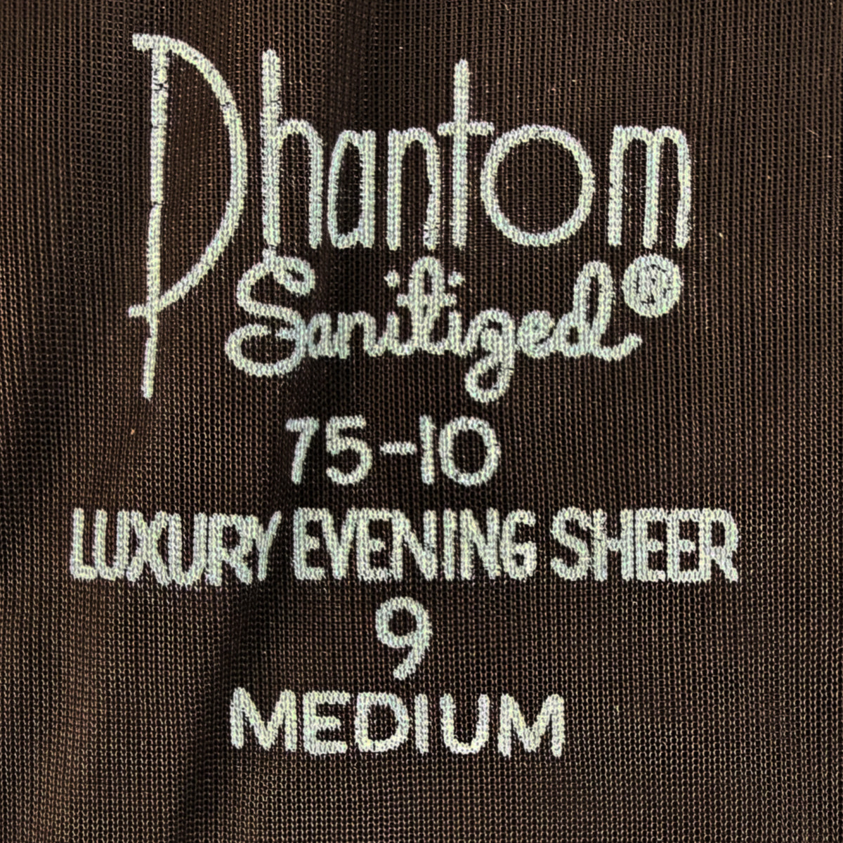 Close-up of a dark brown sheer nylon stocking stamping reading 'Phantom Sanitized 75-10 Luxury Evening Sheer 9 Medium' in white .