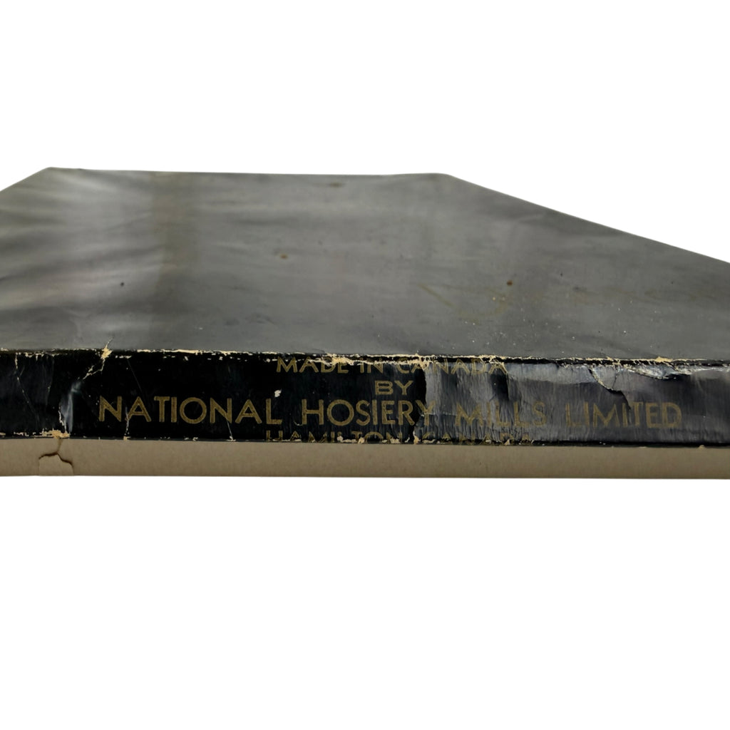A close-up of a vintage black box edge with gold printed text reading 'MADE IN CANADA BY NATIONAL HOSIERY MILLS LIMITED' 