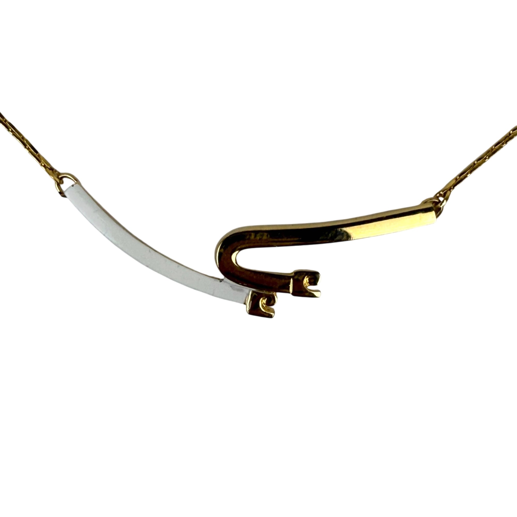 Close-up of gold tone PC monogram pendant with white enamel