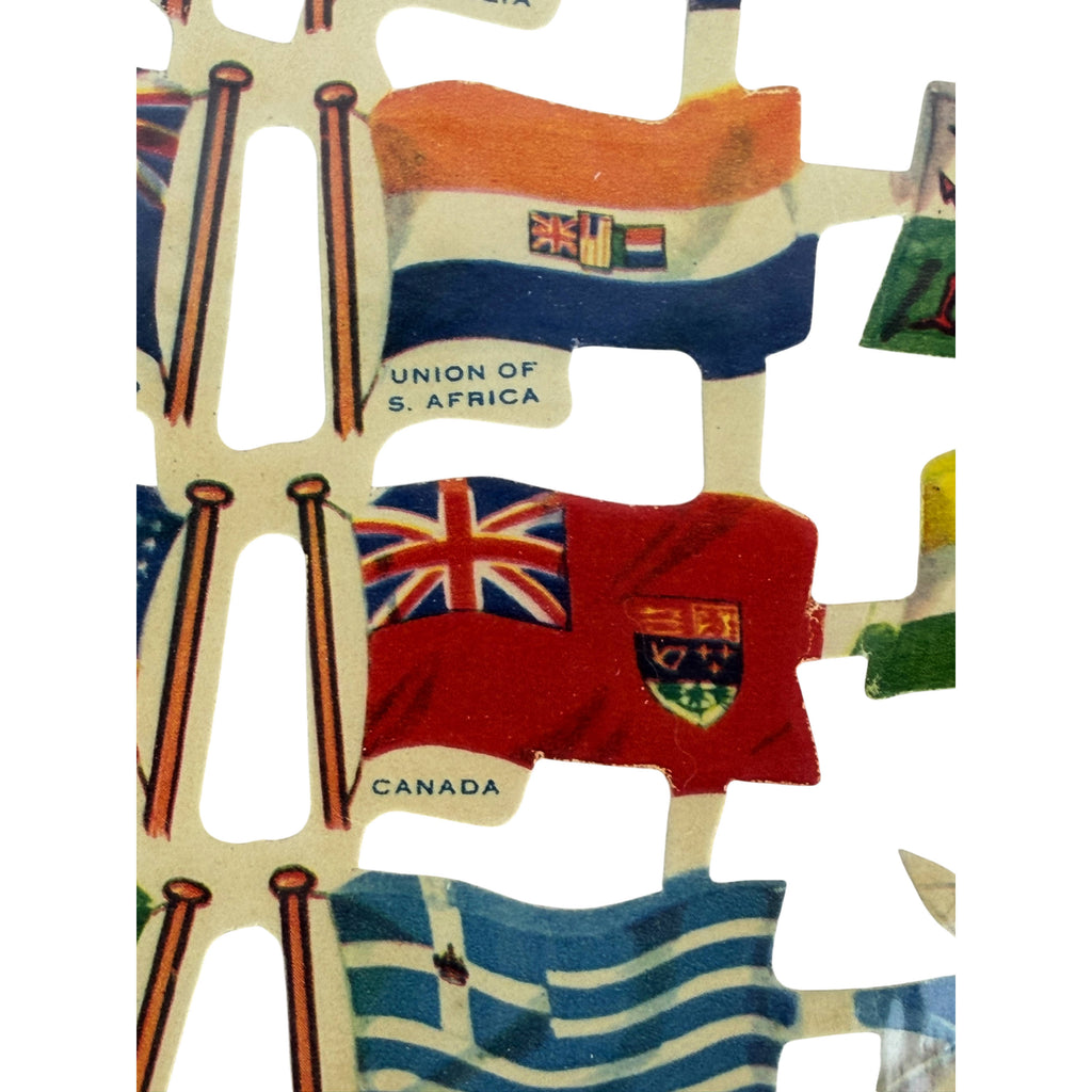 A close-up of vintage diecut paper flags, including the Union of South Africa flag, Canada flag, and other colorful flags on a white background.