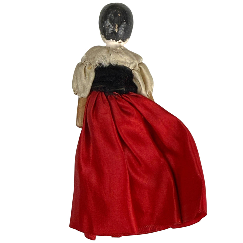 Rear view of 19th-century Grödnertal wooden peg doll showing black painted hair, cream silk blouse and gathered red silk skirt.