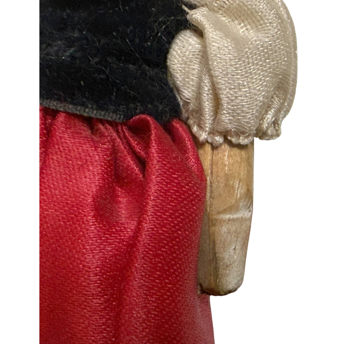 Close-up of antique doll's cream silk puffed sleeve, black velvet bodice, red silk skirt and jointed wooden arm