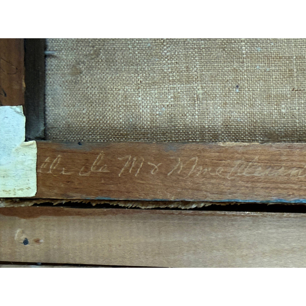 Close-up of the back side of a framed artwork, showing a wooden stretcher bar with faint handwritten inscription and the woven canvas surface behind it.