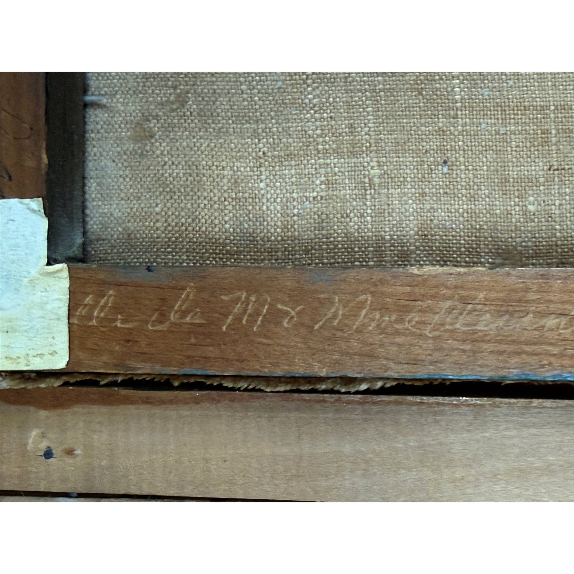 Close-up of the back side of a framed artwork, showing a wooden stretcher bar with faint handwritten inscription and the woven canvas surface behind it.
