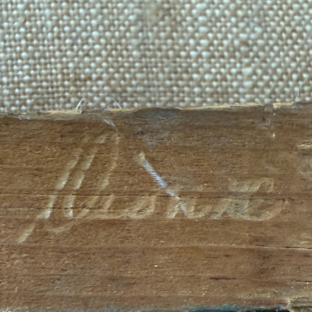 Close-up of a carved wooden surface with a cursive signature and a woven fabric background.