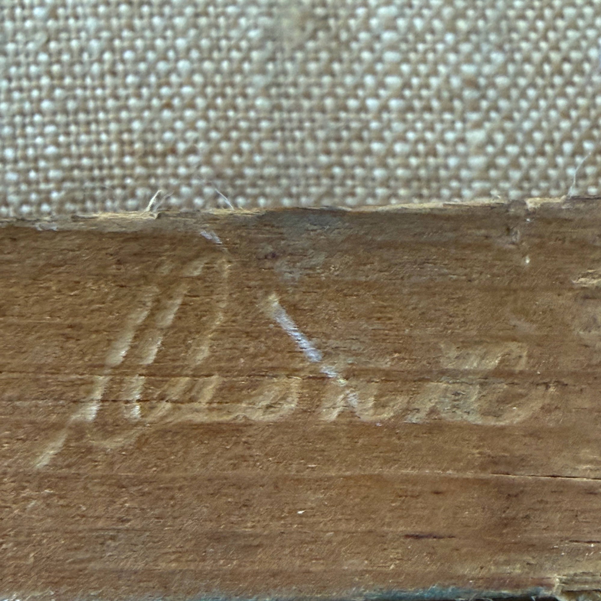 Close-up of a carved wooden surface with a cursive signature and a woven fabric background.