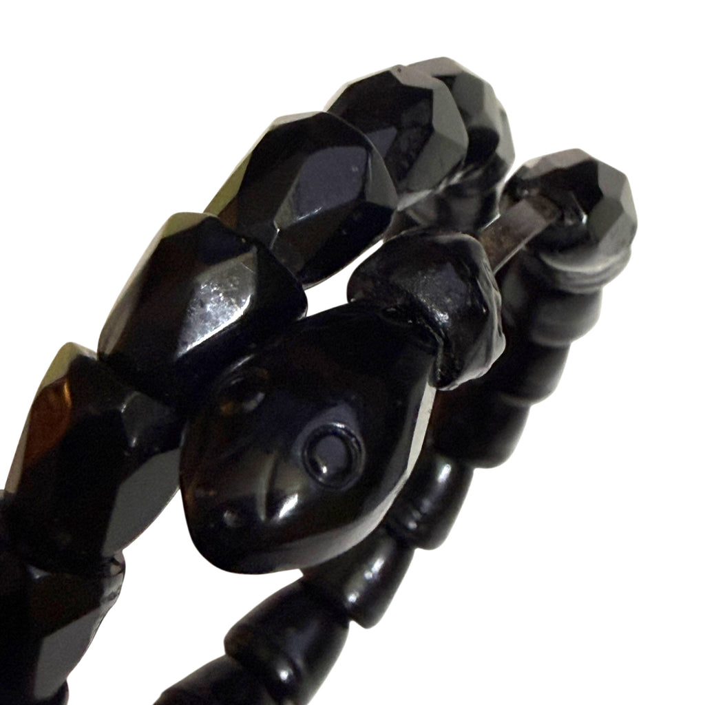 Detailed close-up of sculpted black serpent head on antique Victorian coil bracelet showing circular eye and facial features