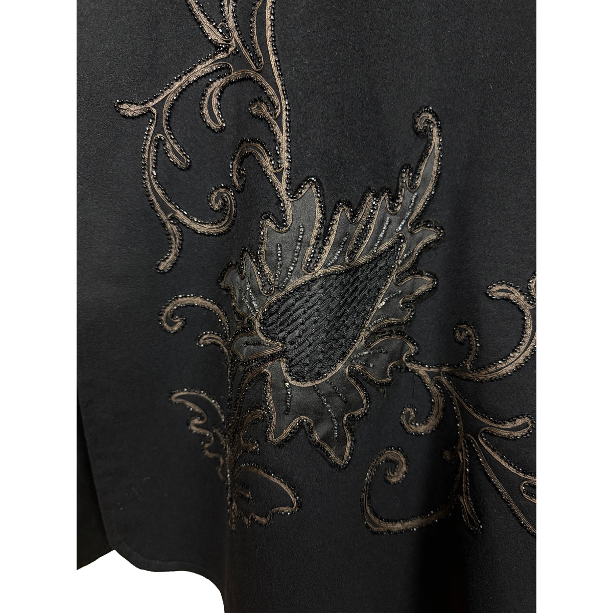Detail of thistle-like floral appliqué and golden-brown corded embroidery on black wool