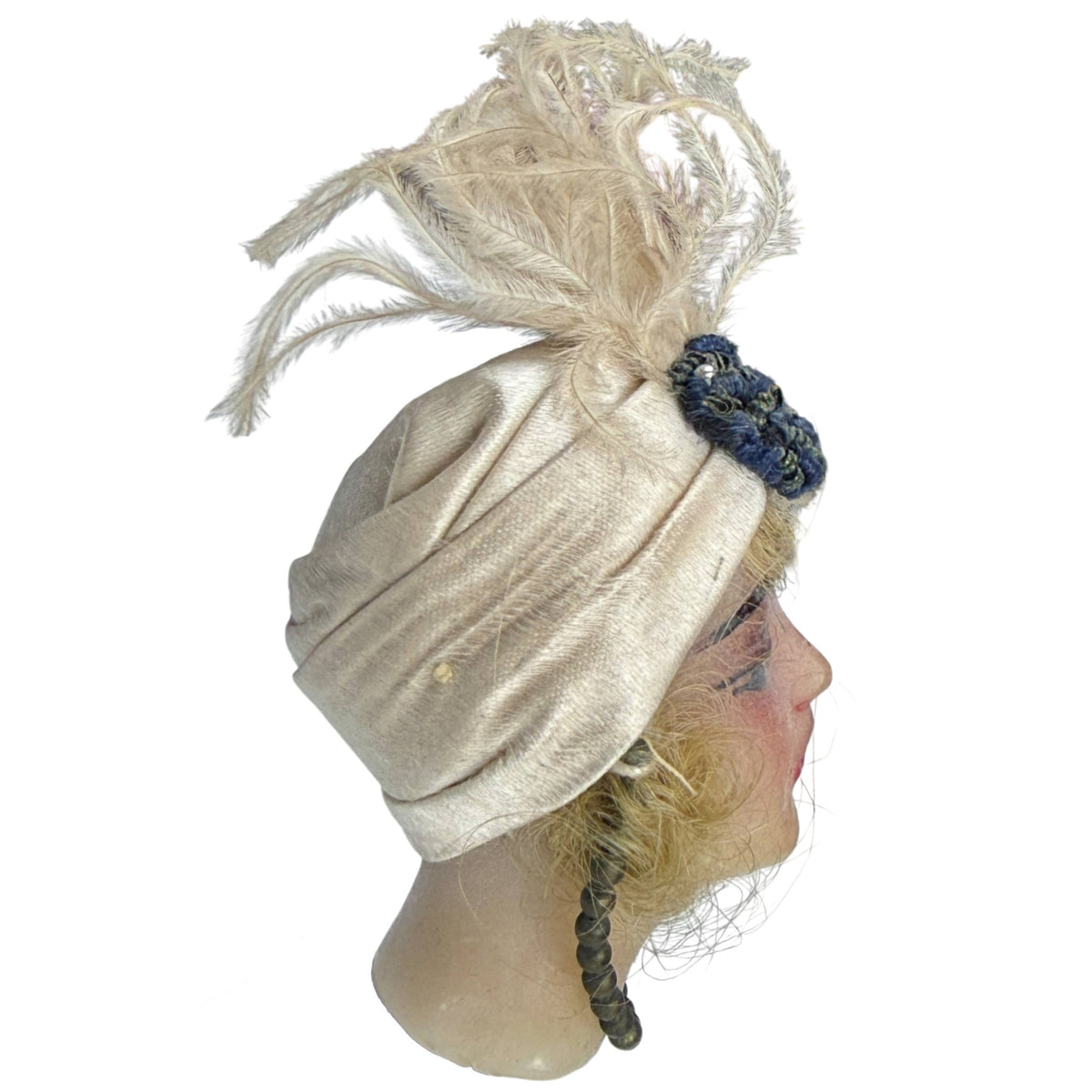 Side profile of antique wax ribbon doll head showing folded satin turban, feather decoration and blonde hair