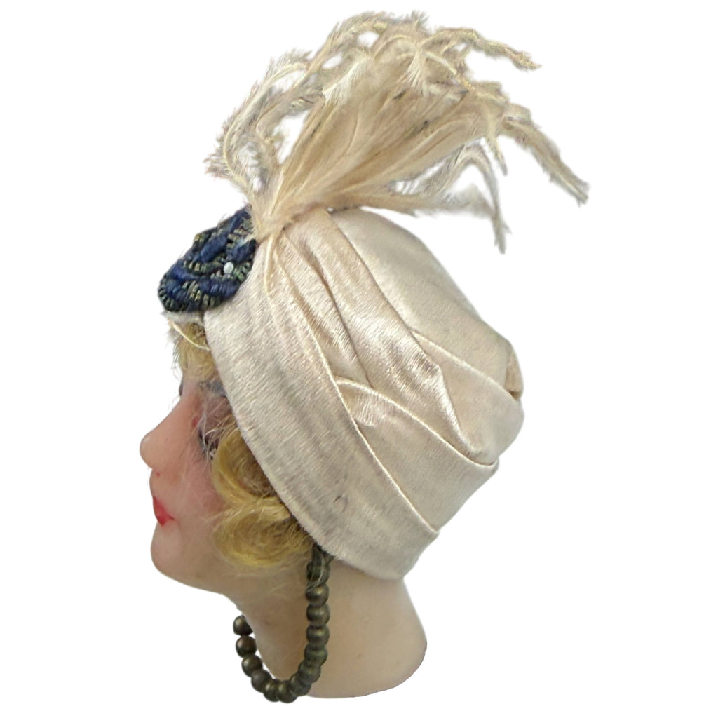 Opposite side profile of antique wax doll head showing layered satin turban, feather plume and metallic bead ornament