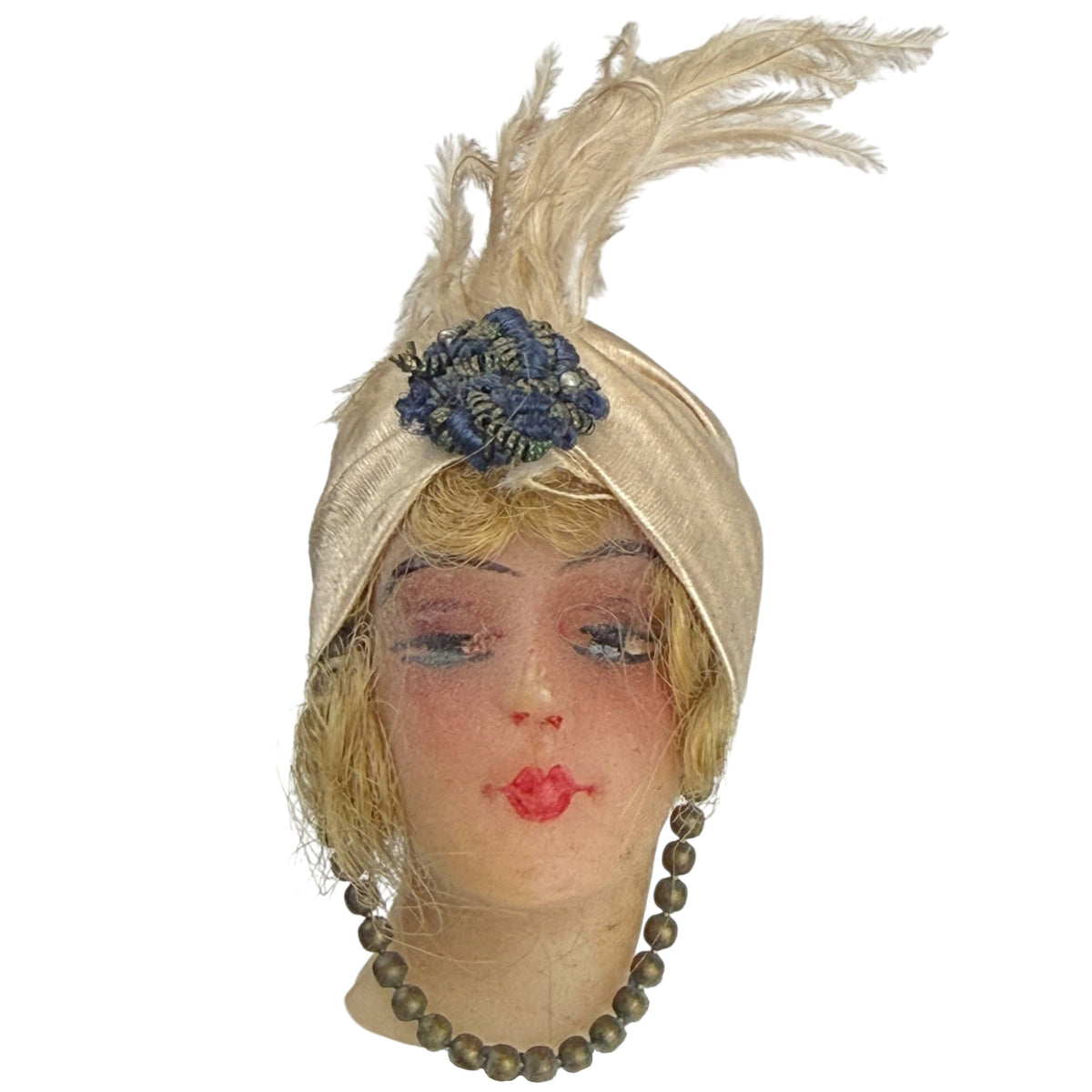 Antique 1910s wax doll head with painted face, blonde hair, champagne satin turban and tall feather plume, front view